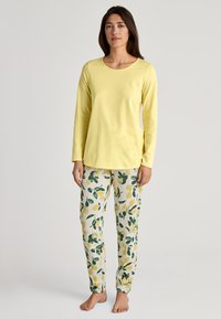 Helles gelbes Langarmshirt, kombiniert mit cremefarbigen Schlafanzughosen, die ein Muster aus Zitronen und grünen Blättern aufweisen. Weiches Baumwollmaterial, lockere Passform.