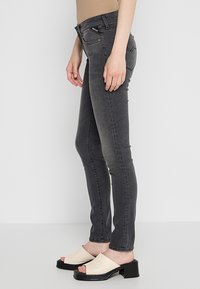 Jeans ajustados grises con una cintura de altura media, un ajuste elegante y un sutil detalle de desgastes. Combinados con sandalias de tacón bloque y punta abierta en color beige.