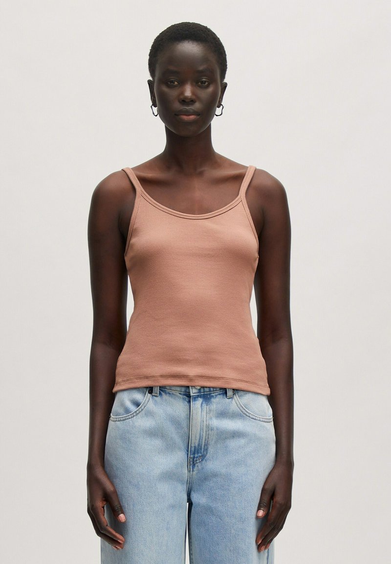 Brauner gerippter Tanktop mit dünnen Trägern, ausgestattet mit einem runden Ausschnitt und einer enganliegenden Silhouette. Kombiniert mit hellblauen, hoch taillierten Jeans.