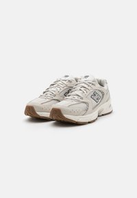 Beige Netz- und synthetische Laufschuhe mit grauen und marineblauen Akzenten. Zu den Merkmalen gehören Schnürsenkel, ein Logo an der Seite und eine strukturierte Gummisohle.