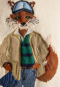 Gestickter Fuchs mit blauer Mütze, beiger Jacke und grün gestreiftem Pullover, der einen geschlossenen Regenschirm vor einem cremefarbenen Strickhintergrund hält.