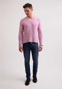 Sweater rosa lavorato a maglia con scollo a V, caratterizzato da polsini e orlo a costine, abbinato a jeans blu scuri e stivali neri alla caviglia. Texture liscia.
