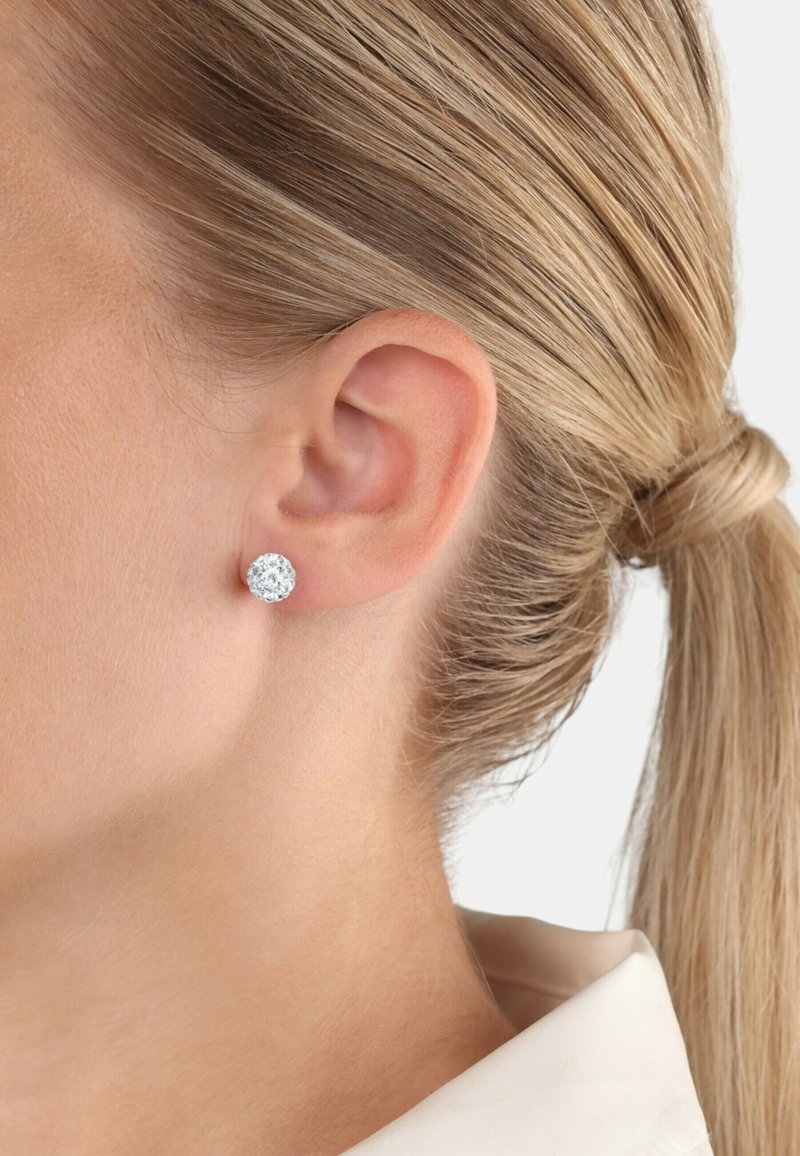 Pendientes de plata en forma de stud con un acabado texturizado y brillante, ajustados de cerca al lóbulo de la oreja, visibles desde el lado de la cabeza de una persona.