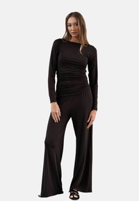 Czarny kombinezon z długim rękawem, z marszczonym wykończeniem w talii, rozszerzonymi nogawkami i gładką, miękką fakturą. Charakteryzuje się minimalistycznym designem.