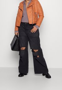 Giacca da biker in finta pelle marrone, polo grigia, jeans neri a gamba larga con grandi strappi e scarpe chunky nere. Borsa a tracolla nera trapuntata.