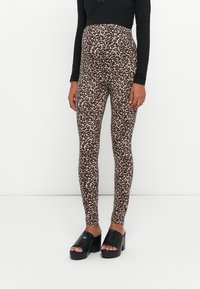 Leggings en imprimé léopard en tissu léger et extensible. Ils ont une taille haute et une texture lisse. Associés à des sandales à plateforme noires.