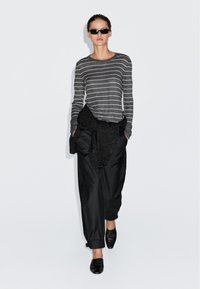 Czarna, w paski szara koszula z długim rękawem w połączeniu z czarnymi spodniami typu high-waisted i czarnymi butami wsuwanymi; modelka wystylizowana z dzianinowym owinęciem wokół talii.