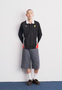 Juodas polo marškinėliai su balta apykakle, raudonomis detalėmis ir logotipu; pilkos šortai; rudi batai; balti kojinės. Paprastas, sportinis dizainas.