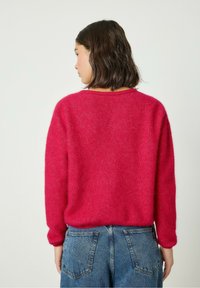 Suéter rosa difuso con mangas largas y un escote redondo, combinado con jeans de mezclilla de tiro alto que presentan bolsillos visibles y costuras.