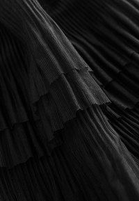 Tissu noir plissé avec une surface texturée, présentant des volants superposés et une qualité en maille, créant profondeur et mouvement.