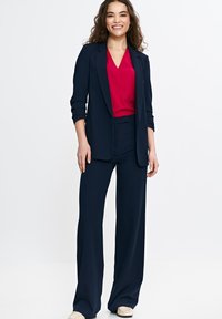 Granatowy garnitur dopasowany, z gładką marynarką i szerokimi spodniami, zestawiony z żywym różowym topem w serek. Gładka tekstura tkaniny.