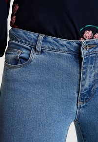 Jeans de mezclilla de color azul claro con un diseño clásico de cinco bolsillos, cierre de cremallera y botón, con detalles de costura visibles y una textura suave.