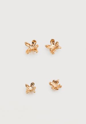 Quatre boucles d'oreilles clous en forme de fleurs couleur or disposées en deux paires sur un fond blanc.