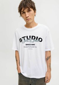 Hvid bomulds t-shirt med sort og teal grafisk tekst: "STUDIO Jack & Jones Siden 1990" og "Designet af J&J teamet." Løs pasform.