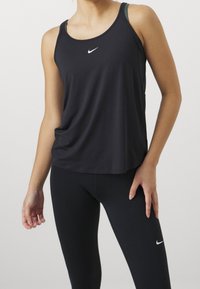 Débardeur de sport noir à encolure ronde, avec un petit logo Nike blanc sur la poitrine. Associé à un legging noir, il met en valeur une silhouette épurée.