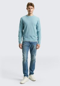 Maglione azzurro chiaro realizzato in morbido materiale a maglia, design con scollo tondo, abbinato a jeans blu sbiaditi e sneakers bianche. Look semplice e moderno.