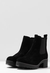 Botas de tobillo de ante negro con un tacón ancho y paneles laterales elásticos, que presentan una superficie texturizada y una puntera redonda.