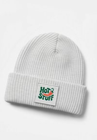 White ribbed beanie with a folded cuff featuring a square patch that reads “HOT STUFF” in green and red lettering with a chili pepper design.