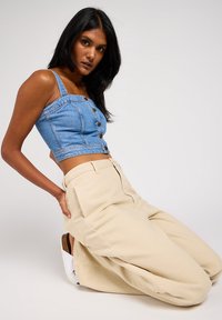 Top de denim recortado con detalles de botones, combinado con pantalones de pierna ancha en color beige. El conjunto presenta un diseño ajustado y una textura suave.