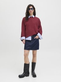 Burgunderfarbener oversized Sweatshirt, das über ein blau-weiß gestreiftes Hemd mit Kragen getragen wird, kombiniert mit einem Jeansrock und schwarzen kniehohen Stiefeln.