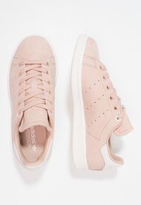 Ett par ljusrosa Adidas Stan Smith-sneakers med vita sulor, sedda från ovan och sidan mot en vit bakgrund.