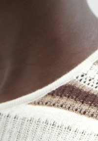 Knit sweater with a cream base, featuring vertical stripes in brown and beige. The neckline is wide with a textured, open weave.