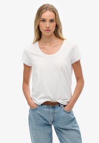 Hvid, kortærmet t-shirt med rund halsudskæring, lavet af et blødt materiale; parret med lyseblå, løstsiddende jeans og et brunt vævet bælte.