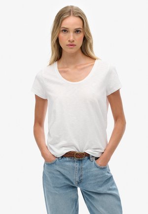 Witte T-shirt met korte mouwen en een ronde hals, gemaakt van een zachte stof; gecombineerd met lichtblauwe, losse spijkerbroek en een bruine gevlochten riem.