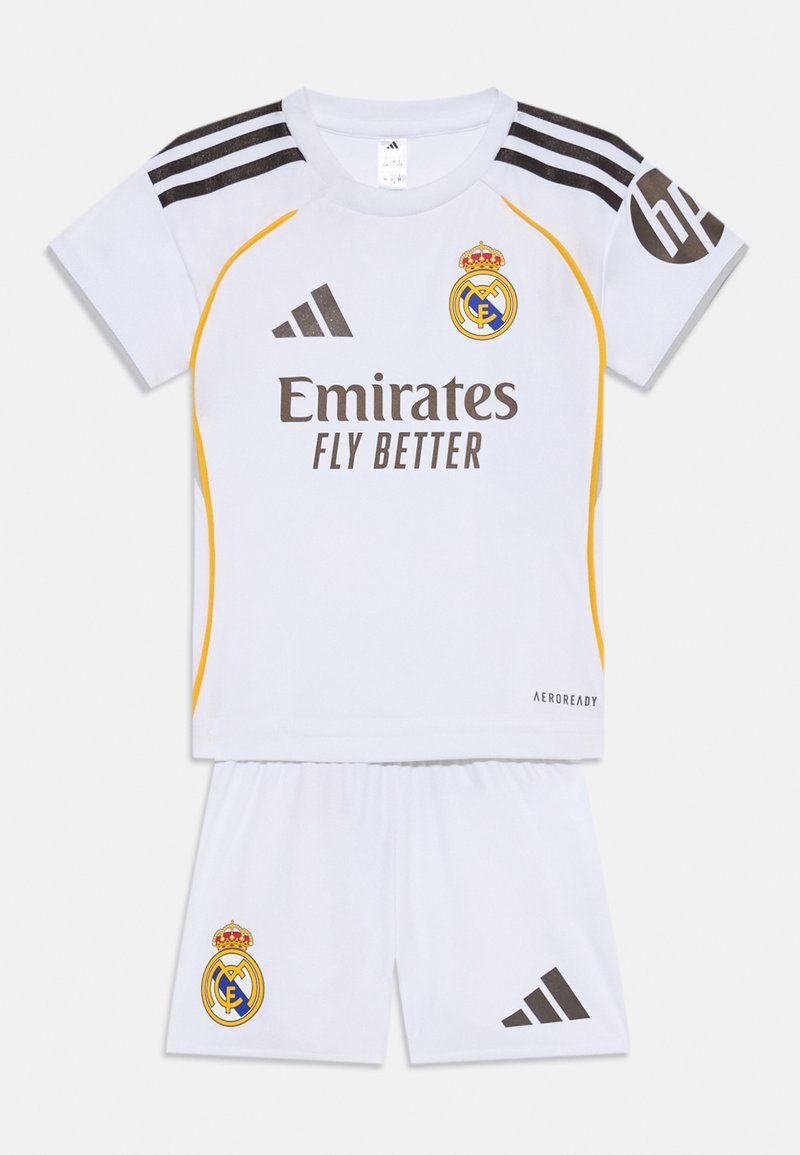 Weißes Fußballtrikot bestehend aus einem kurzärmeligen Shirt und Shorts, mit schwarzen und gelben Akzenten, Adidas-Logo und Real Madrid-Wappen.