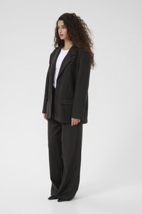 Černý oversized blazer se dvěma knoflíky a klopovými kapsami, doplněný volnými černými kalhotami a upnutým bílým tričkem. Hladká textilie.