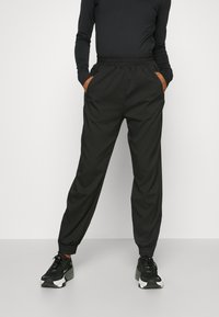 Black jogger pants with an elastic waistband, side pockets, and tapered cuffs. Made from lightweight fabric, featuring a smooth texture.