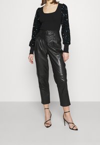 Haut noir côtelé avec manches bouffantes ornées de sequins, associé à un pantalon en cuir noir taille haute et des talons noirs à lanières.