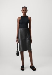 Haut noir sans manches, design ajusté. Jupe midi en cuir noir avec une texture lisse. Sandales à plateforme noires et petit sac à main avec une bandoulière.