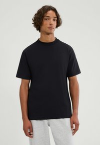 Czarna bawełniana koszulka z krótkim rękawem, z okrągłym dekoltem i subtelnym haftowanym logo na piersi, o luźnym kroju i miękkiej fakturze.