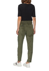 Grüne, gemusterte Hose mit elastischem Bund, zwei Gesäßtaschen und schmaler Form, kombiniert mit einem schwarzen T-Shirt mit kurzen Ärmeln und weißen Sneakern.