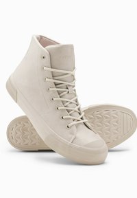 Zapatillas altas beige hechas de cuero suave con punta redonda y suela de goma texturizada. Presentan ojales y cordones a juego para un ajuste seguro.