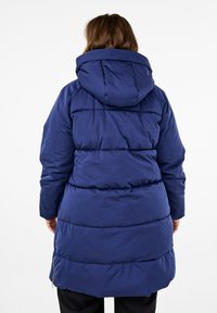 Navyblauwe pufferjas met een capuchon, voorzien van doorstikte panelen en een middellange lengte. Inclusief zijritsen en een zachte textuur.