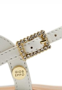 Sandale en cuir blanc avec une sangle dotée d'une boucle rectangulaire en or ornée de cristaux transparents, et un disque de logo marqué "GIOS EPPO."