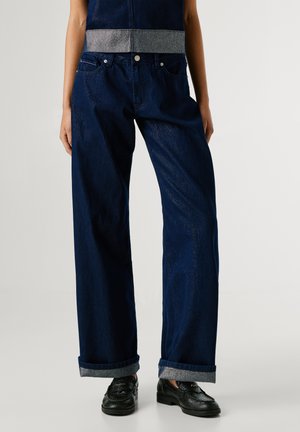 Jeans de tiro medio de gran ancho en azul oscuro, con detalles plateados en la cinturilla y puños remangados con tela interior en contraste.