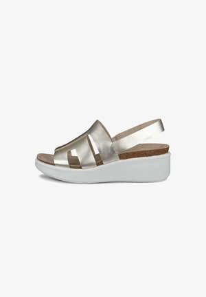 Sandales métalliques dorées avec une sangle élastique, semelle en liège et semelle plate blanche. Design ouvert à l'avant avec des découpes.