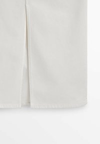 Jupe en tissu blanc avec une fente centrale dévoilant un panneau intérieur superposé, ourlet droit et couture visible.