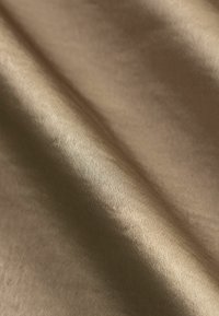Λείο, διπλωμένο μπεζ ύφασμα με ορατή λεπτή υφή και απαλά σκιάδια που αναδεικνύουν τις πτυχώσεις και τα διπλώματα.