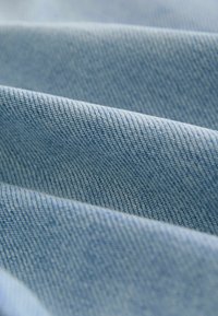 Țesătură din denim de un albastru deschis, cu o textură netedă, având ușoare modele în diagonală de tip twill și variatii subtile de culoare.