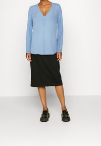 Top azzurro chiaro a maniche lunghe con scollatura a V, abbinato a una gonna nera lunghezza ginocchio e scarpe col tacco piattaforma nere. Tessuto liscio e morbido.