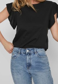 Černý krátký rukáv top z lehkého materiálu, v kombinaci se světle modrými džíny s vysokým pasem, které mají přední kapsy a kovové zapínání na knoflík.