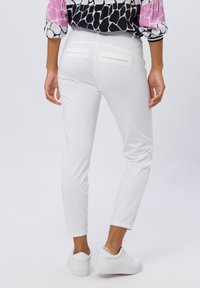Witte stretchbroek met een slanke pasvorm en enkel lengte, voorzien van twee achterzakken en gecombineerd met witte sneakers. Glad textuur.