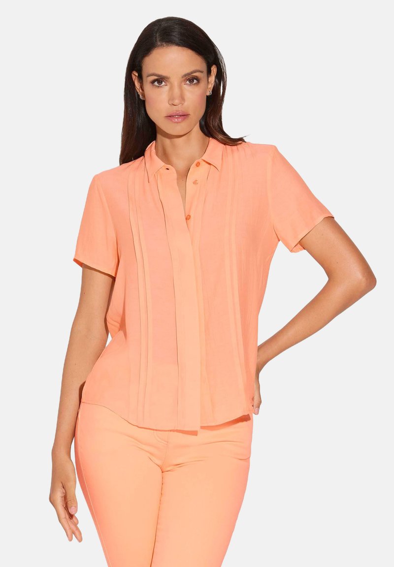 Korte mouwen perzikblouse met verticale plooien, knoopsluiting en een relaxed fit. Gemaakt van lichtgewicht, zachte stof.