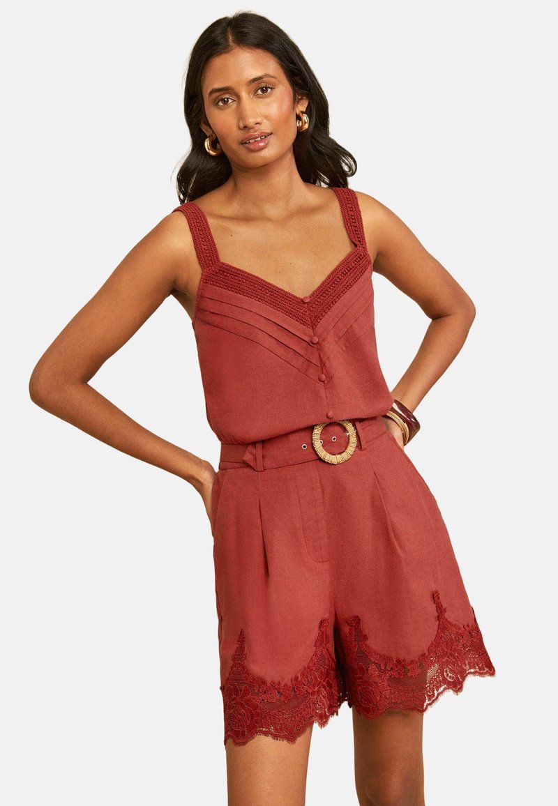 Woman wearing rust-colored sleeveless top with button details and matching high-waist shorts with lace trim and woven belt buckle.
