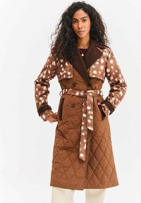 Brązowy pikowany płaszcz z wzorem zamszowego futra w cętki na rękawach i górnej części, z szerokim kołnierzem, paskiem i podwójnymi guzikami.