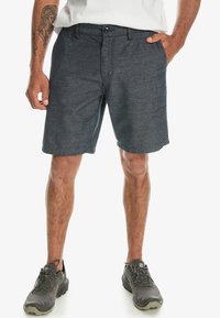 Herrshorts i mörkgrått i en texturerad tyg, med knappstängning, bältesöglor och sidofickor. Bärs med grå sportskor.